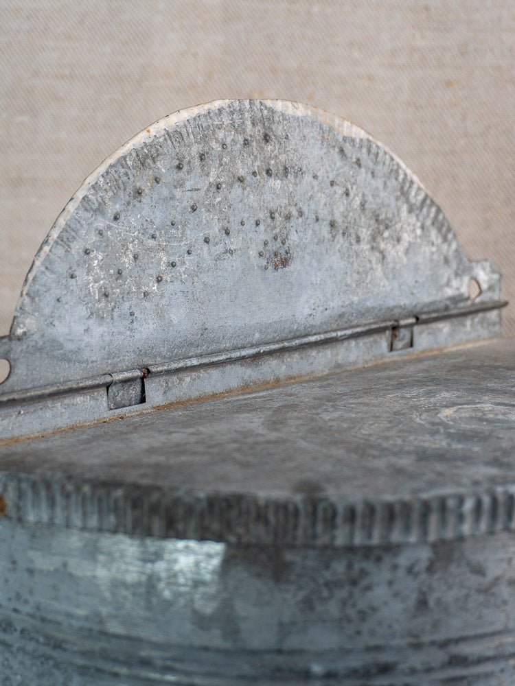 Close-up of weathered galvanized metal hinge on antique French zinc wall fountain with brass tap.
