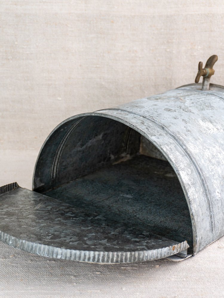 Antique French zinc wall fountain with brass tap, lid open to reveal interior on beige surface.