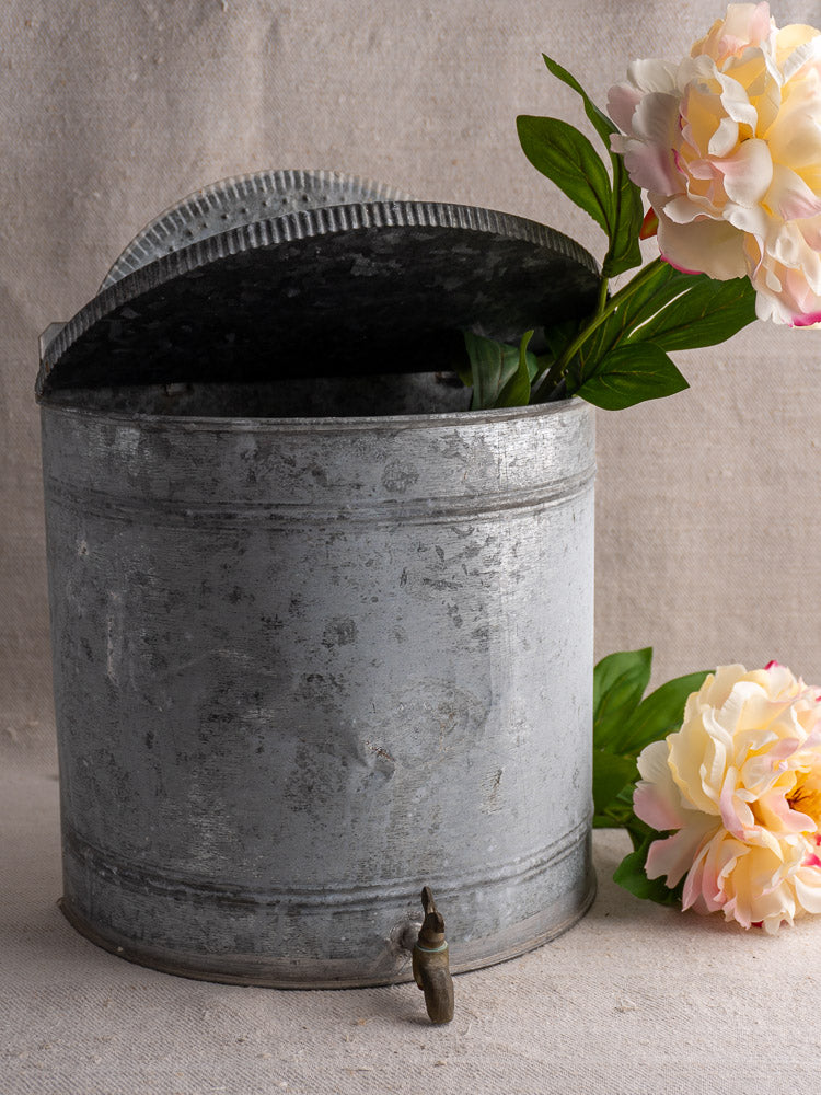 Antique French zinc wall fountain lavabo with ribbed semicircular back and brass tap, neutral fabric backdrop.