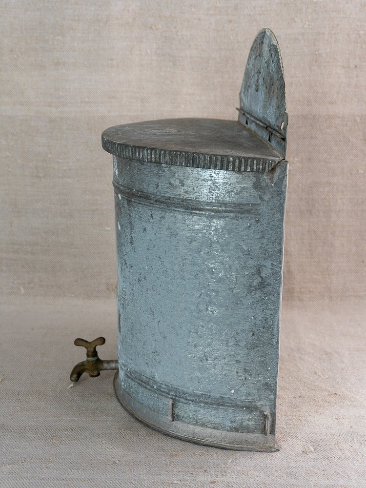 Antique French zinc wall fountain with brass tap, early 20th century, on beige fabric surface.