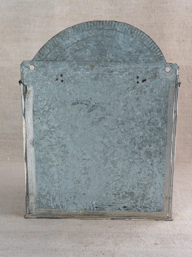 Antique French zinc wall fountain with brass tap, early 20th century, on beige fabric background.
