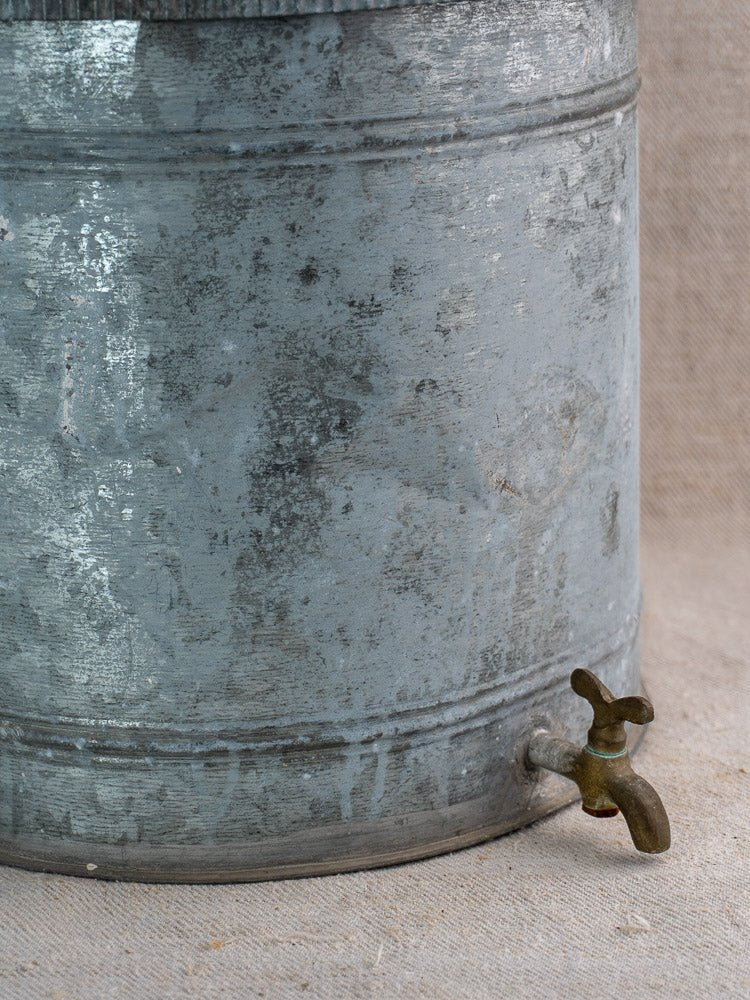 Antique French zinc wall fountain with brass tap, early 20th century, on beige fabric background.