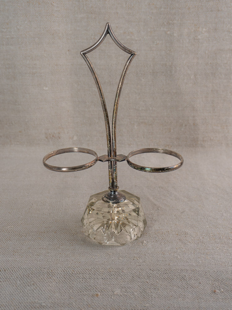 Antique French silver plate and cut glass condiment server with ornate handle, on beige textured fabric.