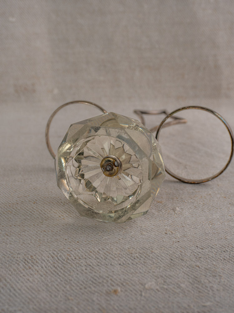 Vintage glass drawer knob with metal screw on beige textured fabric, two metal rings behind.
