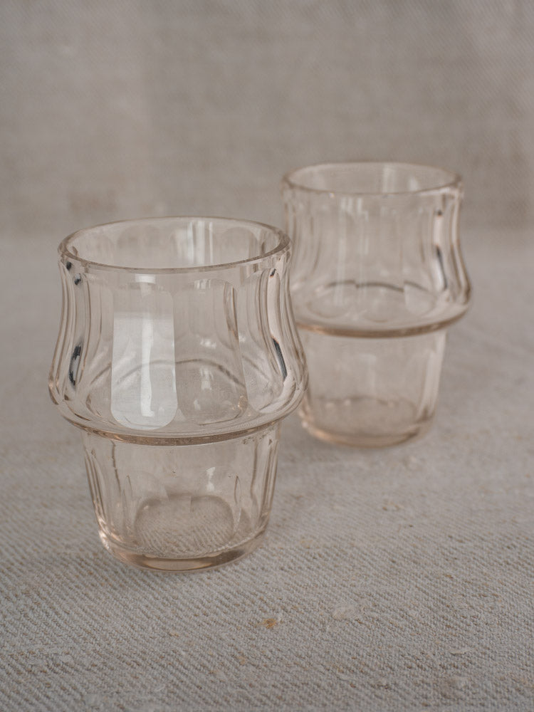 Two clear, textured drinking glasses with wavy, flared sides on a light fabric backdrop.