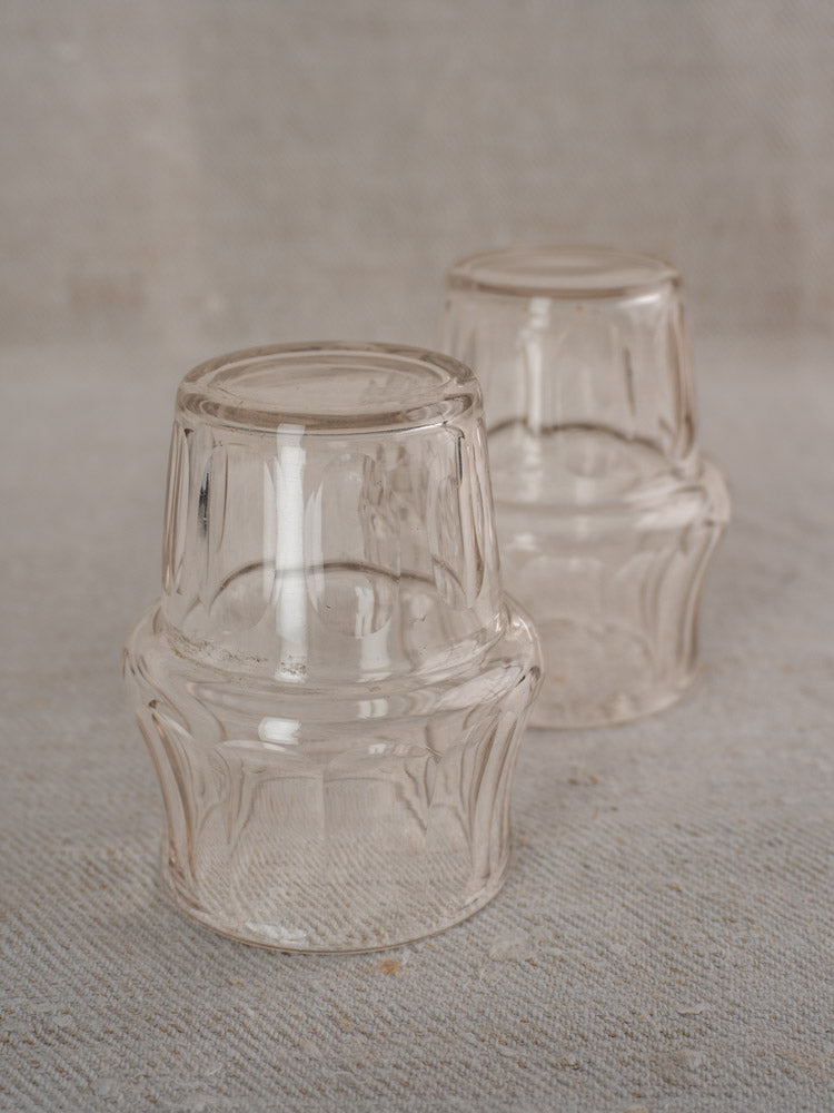 Pair of cut glass cups from an antique French condiment server, upside down on beige fabric.