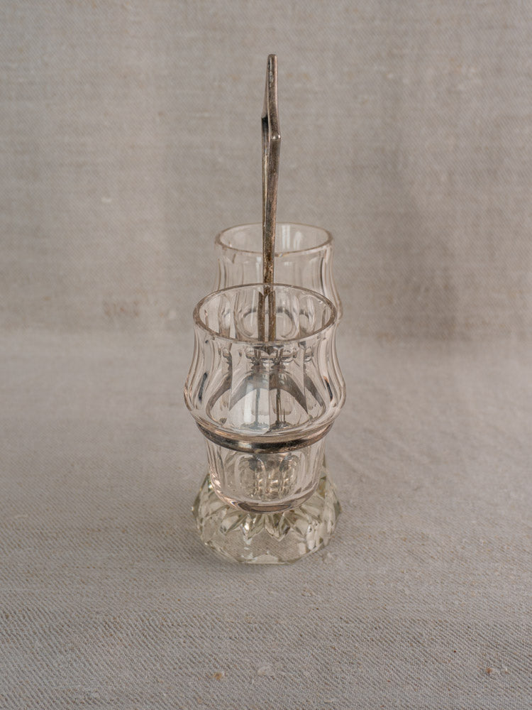 Antique French silver plate and cut glass condiment server with two small glass cups on a fabric backdrop.