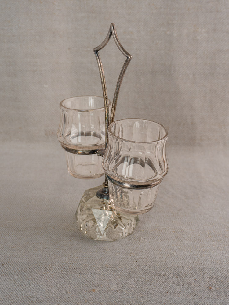 Antique French condiment server with silver plate frame and two curved cut glass holders on neutral fabric.