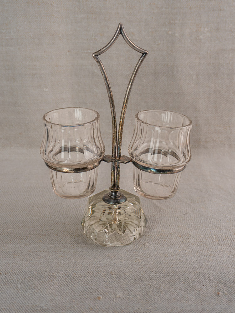 Antique French silver plate and cut glass condiment server with dual cups on cut glass base, neutral fabric backdrop.