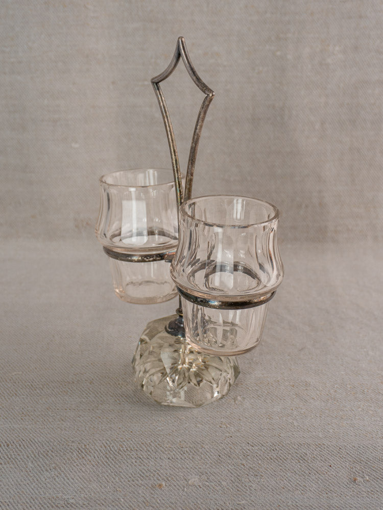 Antique French silver plate and cut glass condiment server on vintage metal stand, light gray fabric background.