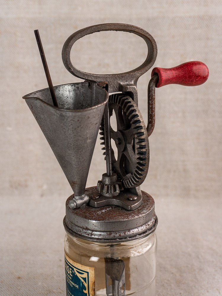 Antique French FUPA Vitesse Baratte mayonnaise maker with hand crank and glass jar on fabric background.