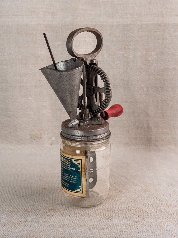 Antique French FUPA Vitesse Baratte mayonnaise maker with metal crank and glass jar on neutral fabric.