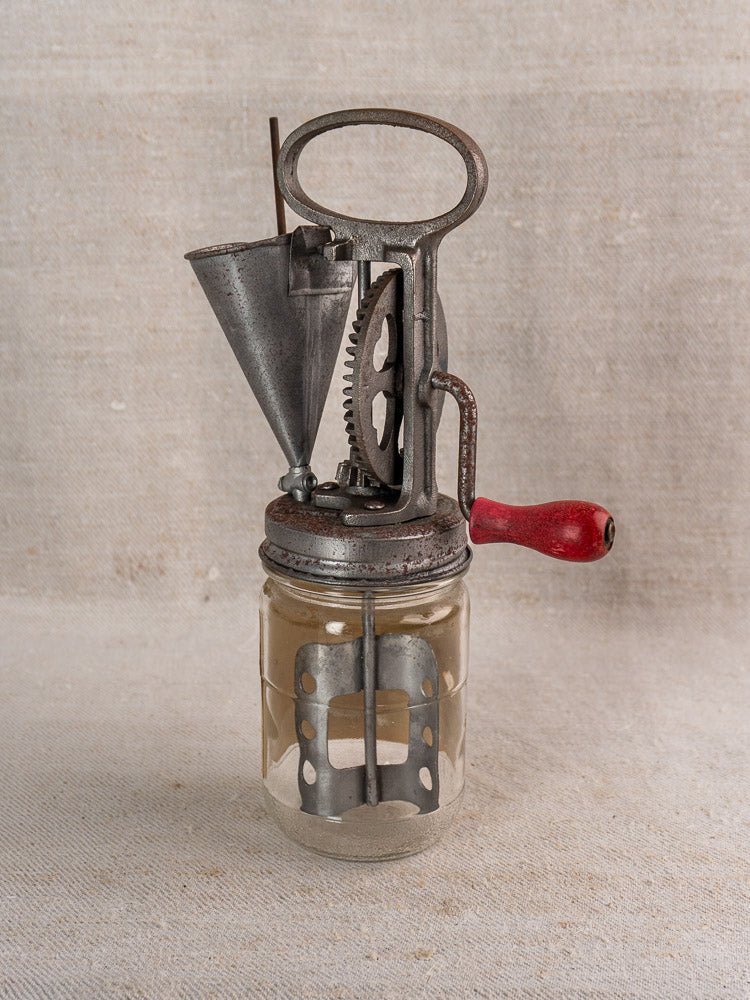Antique French FUPA mayonnaise maker, Vitesse Baratte, with glass jar and red handle on neutral fabric.