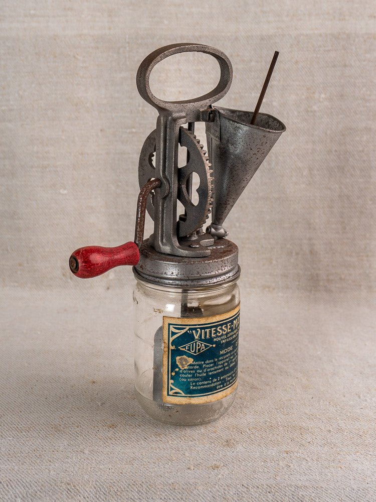 Antique French Vitesse mayonnaise maker, metal and glass with gears and funnel, on beige textured surface.