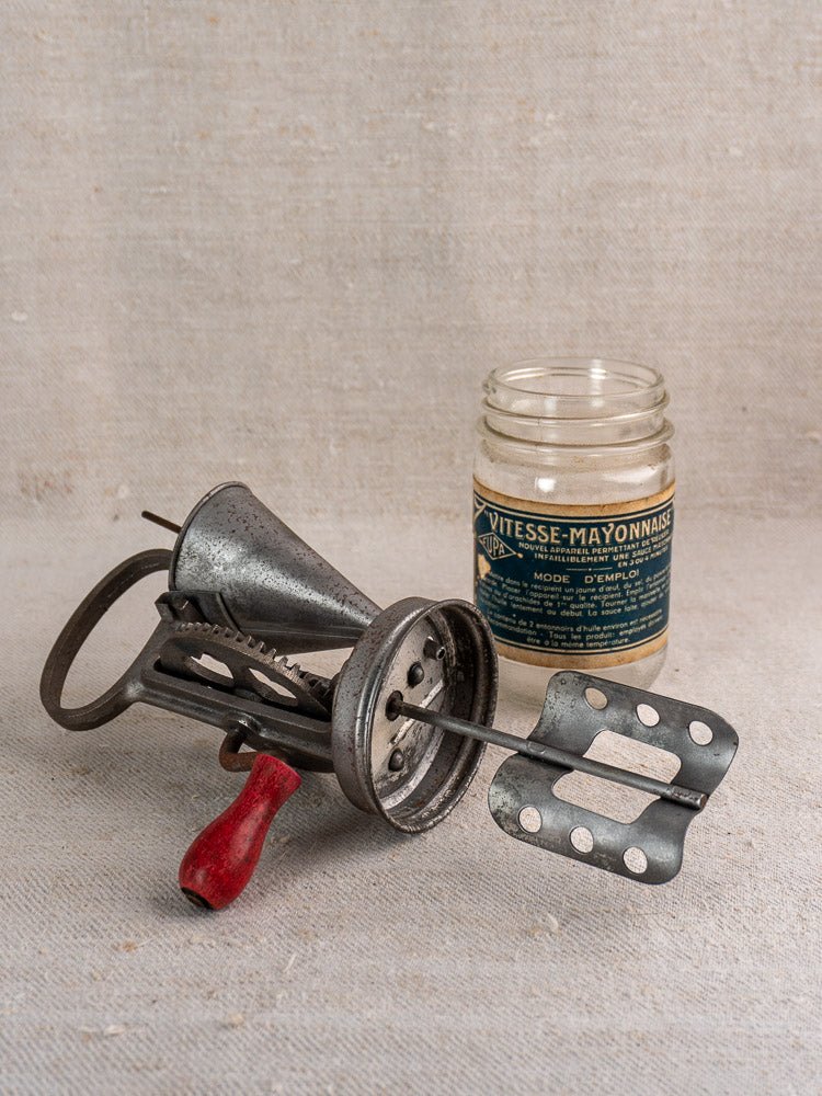 Antique French Vitesse Baratte mayonnaise maker with red-handled beater and labeled glass jar on fabric.