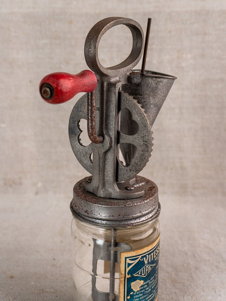 Antique French FUPA mayonnaise maker, Vitesse Baratte c. 1920s, metal tool with red handle on glass jar, plain light background.