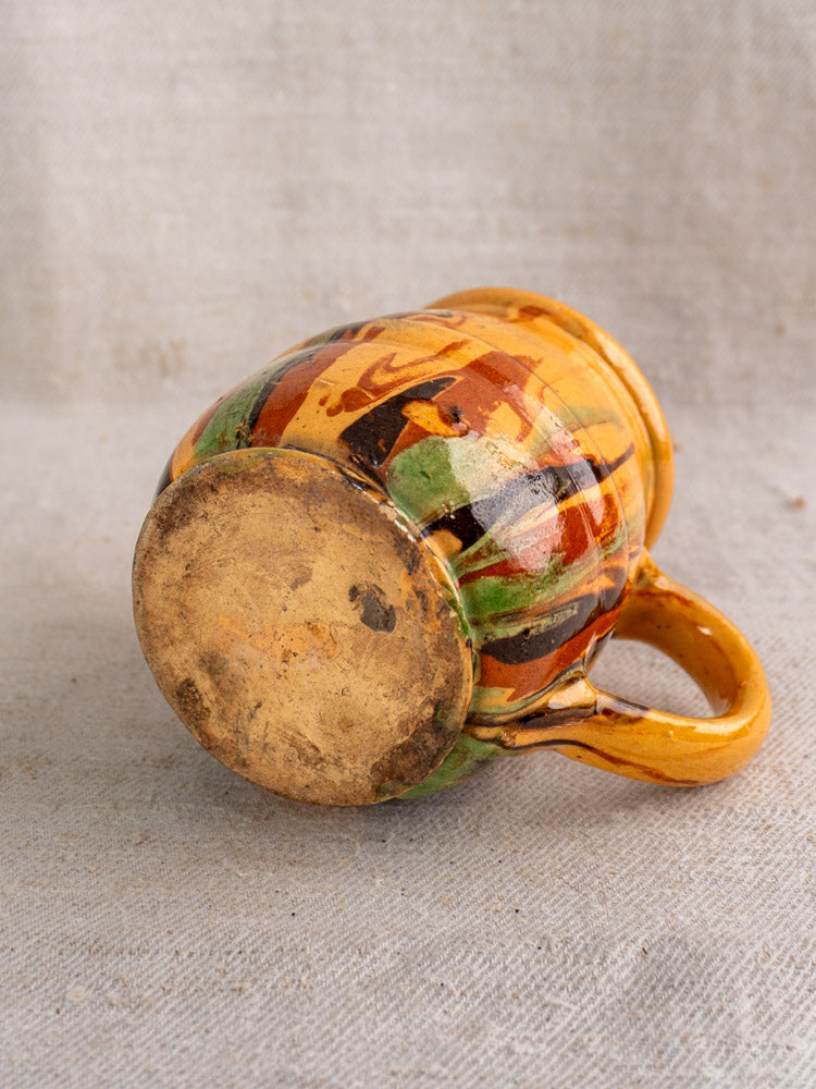 Antique French Jaspé pitcher, hand-thrown with yellow, green, brown, and orange slip glaze showing unglazed base. Late 19th century.