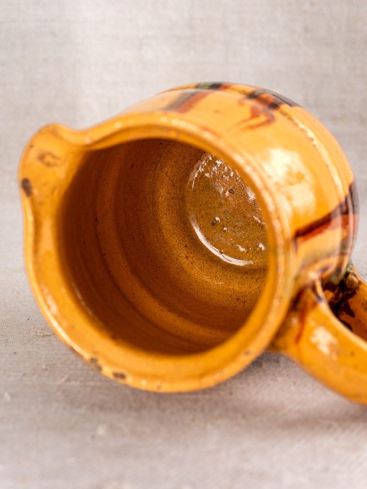 Antique French Jaspé pitcher, late 19th century, hand-thrown slip-glaze, handle and interior visible on neutral fabric.