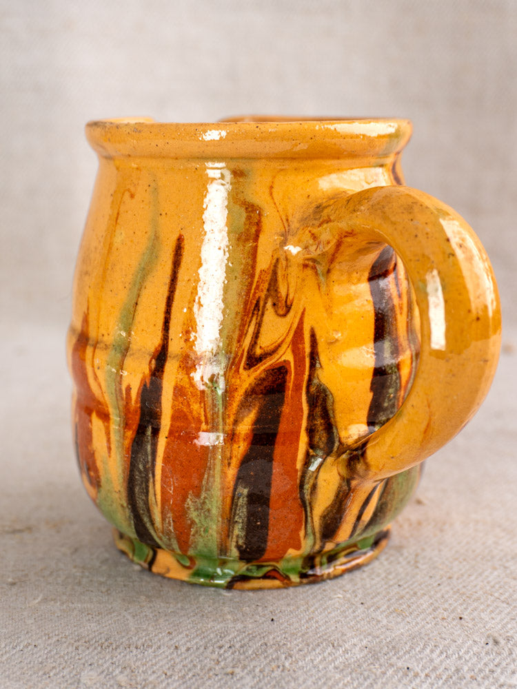 Antique French Jaspé ceramic pitcher with marbled orange, brown, green, and yellow glaze on neutral fabric background.