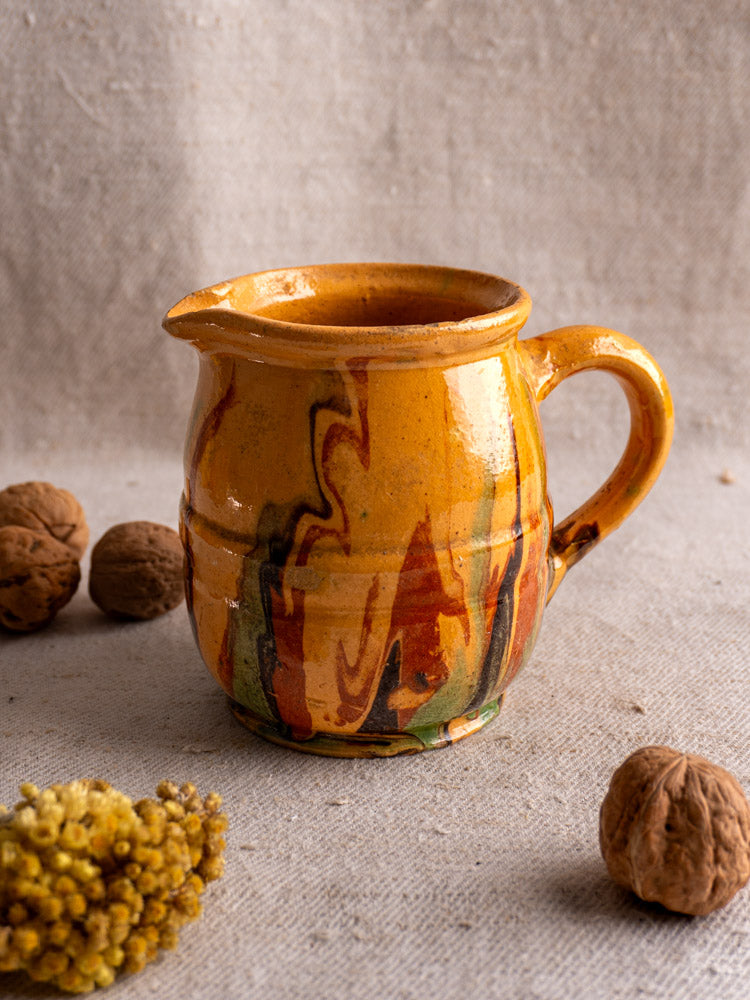 Antique French Jaspé pitcher with marbled orange, red, and green slip glaze next to walnuts and yellow dried flowers.