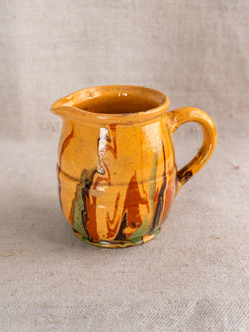 Antique French Jaspé pitcher with yellow-brown glaze and marbled streaks on a neutral fabric background.