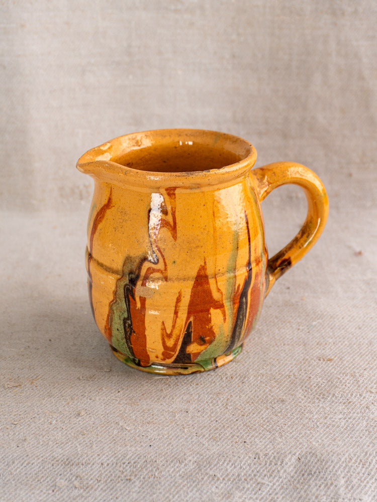 Antique French Jaspé pitcher with yellow-brown glaze and marbled streaks on a neutral fabric background.