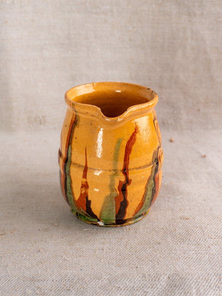 Antique French Jaspé ceramic pitcher with orange, brown, and green stripes on neutral textured fabric, late 19th century.