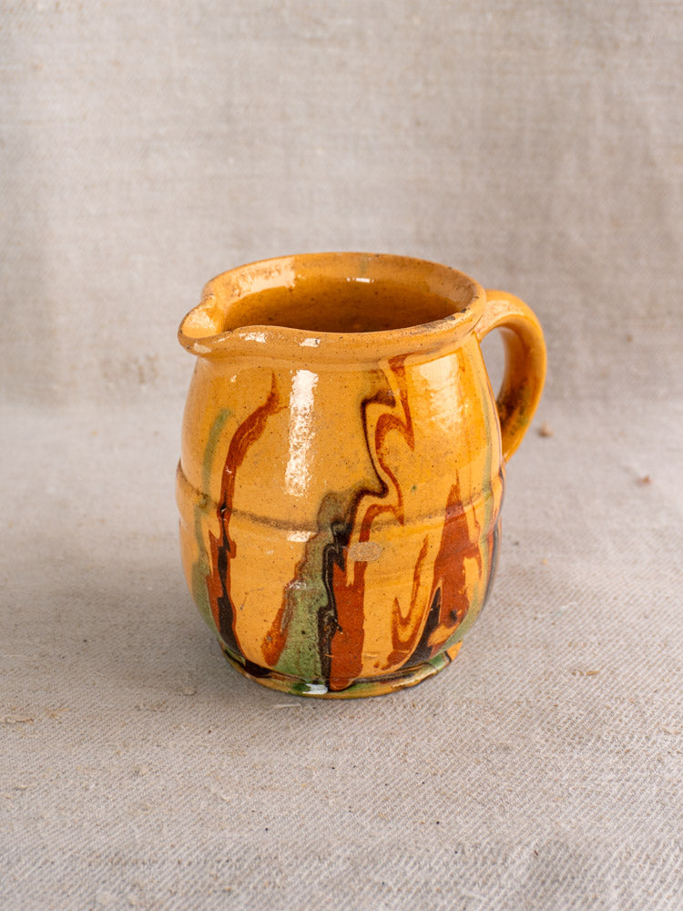 Antique French Jaspé pitcher with glossy yellowish-brown slip glaze, late 19th century, on beige fabric.