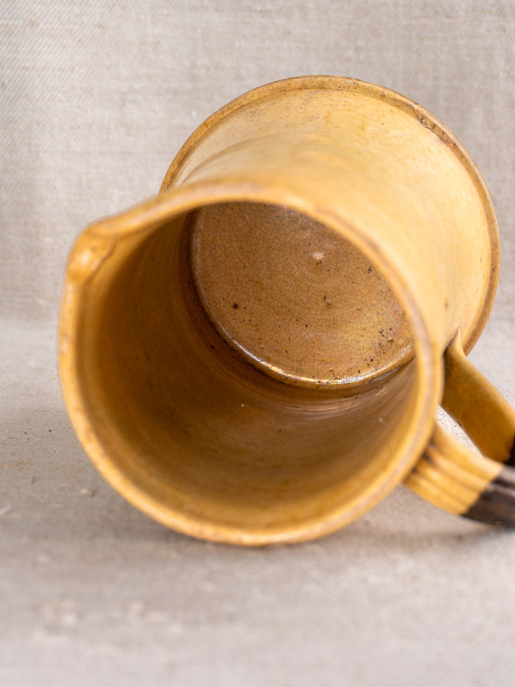 Antique French Pichet Jaune, yellow glazed earthenware pitcher, showing handle and interior on beige textured fabric.