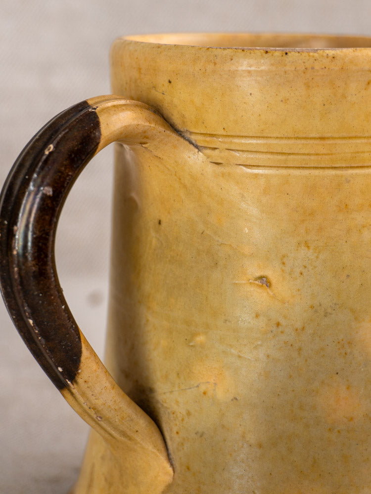 Antique French Pichet Jaune, late 19th-century yellow glazed earthenware mug with textured surface and dark brown handle.