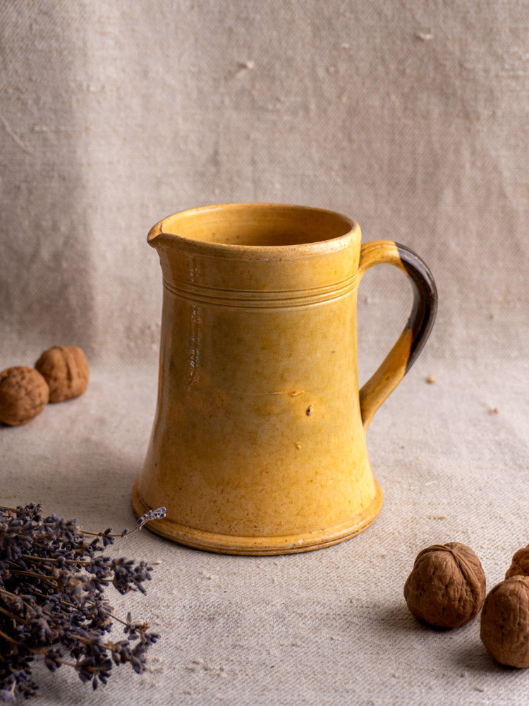 Antique French yellow glazed earthenware pitcher displayed on beige cloth with walnuts and dried lavender.