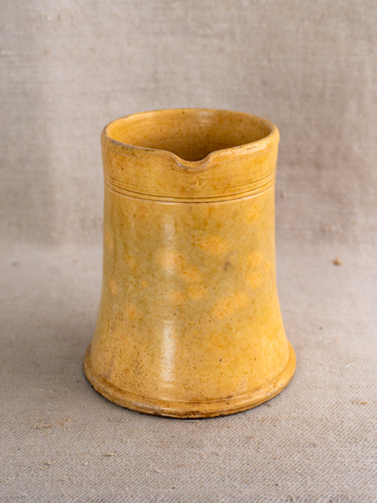 Antique French Pichet Jaune yellow glazed earthenware pitcher with cylindrical shape and line details on beige fabric.