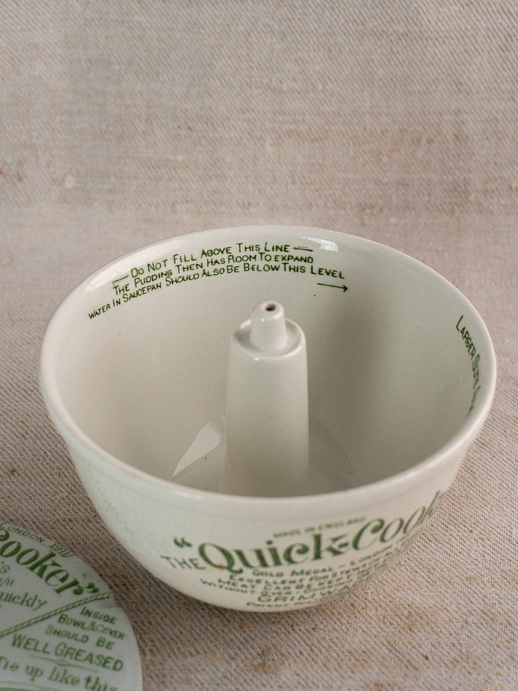 Antique English ironstone pudding steamer with central column and green script, displayed on neutral fabric.