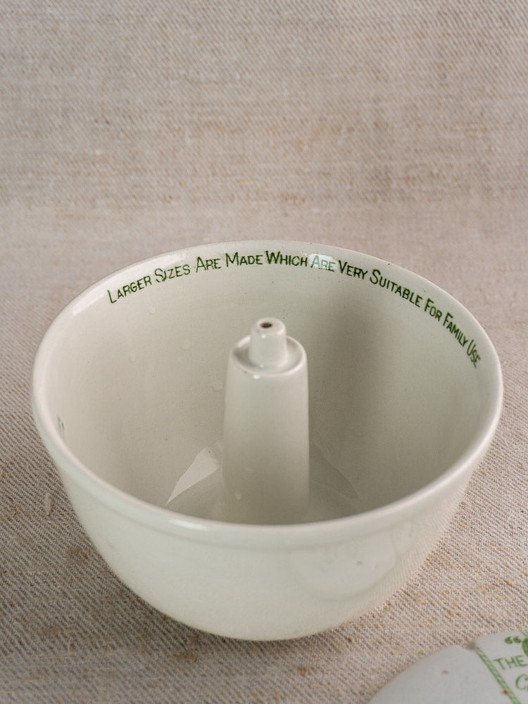 Antique Grimwade Quick Cooker c.1911, white ceramic pudding steamer with green rim script, on textured beige surface.