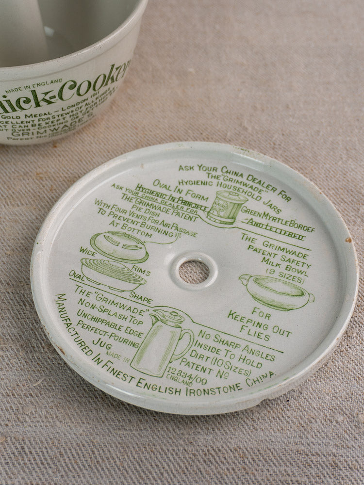 Antique Grimwade Quick Cooker ceramic lid, c.1911, with green script and illustrations, beside matching jug on beige surface.