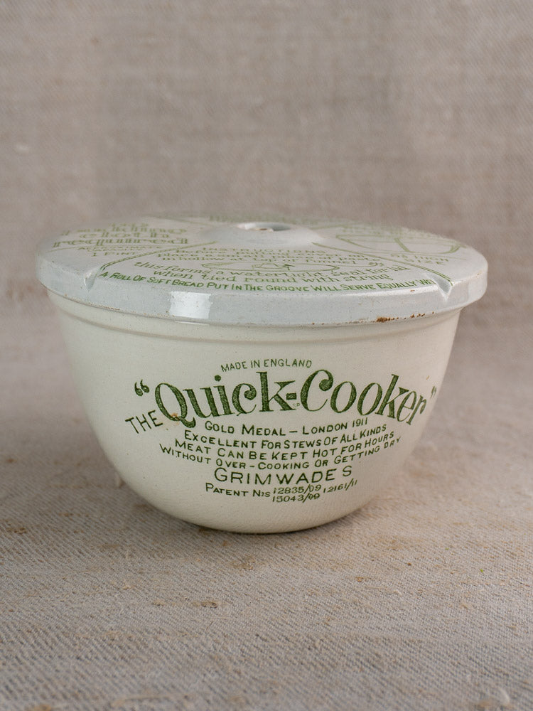 Antique English Grimwade Quick Cooker pudding steamer with fitted lid and green label on textured beige fabric.