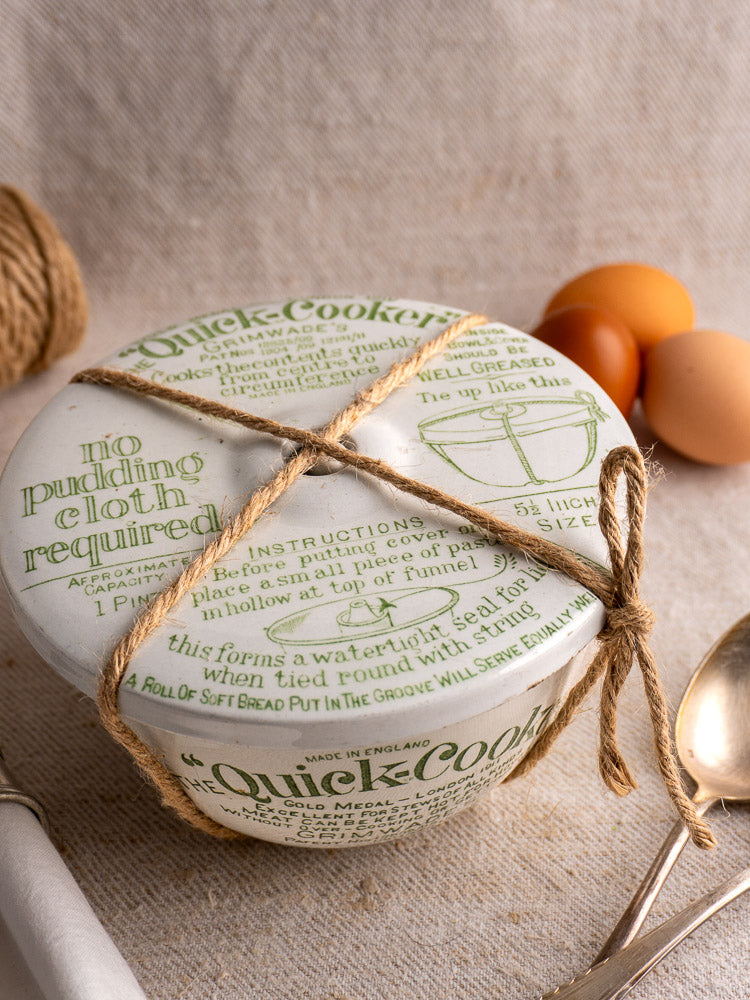 Antique English Grimwade Quick Cooker pudding steamer with green script, tied with twine, eggs and spoon nearby.