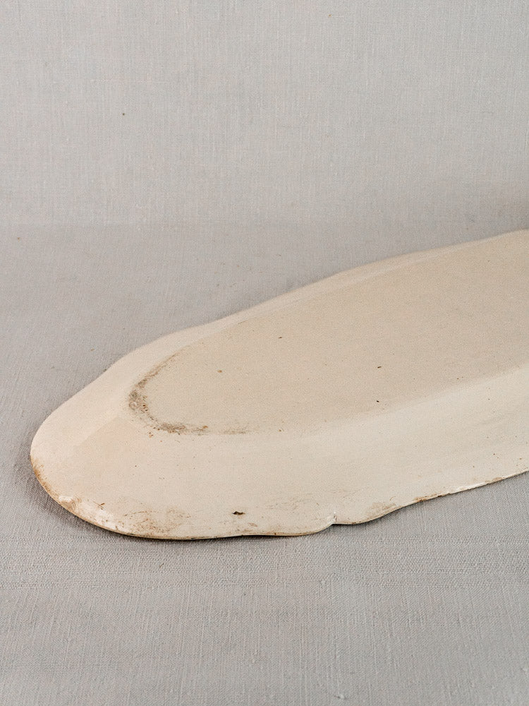 Early 19th-century French faience meat platter with creamy glaze and subtle age patina on gray surface.