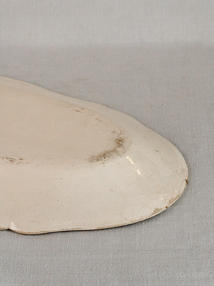 Off-white French faience meat platter with glossy finish and light wear, on gray fabric background.