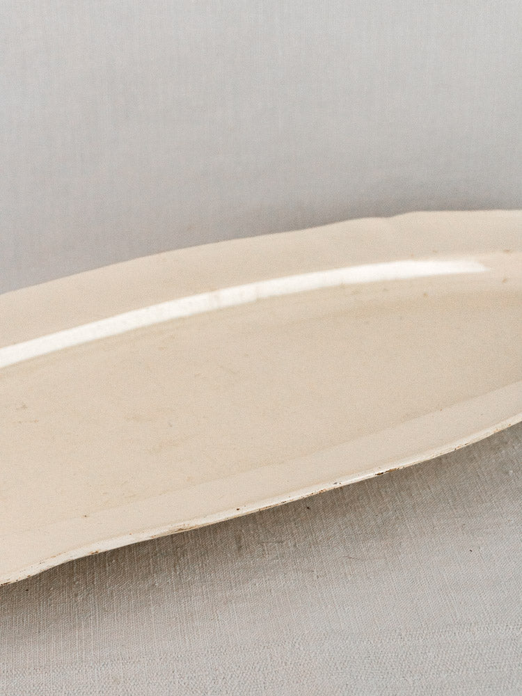Antique French faience oval meat platter, off-white ceramic, on a light gray textured surface.