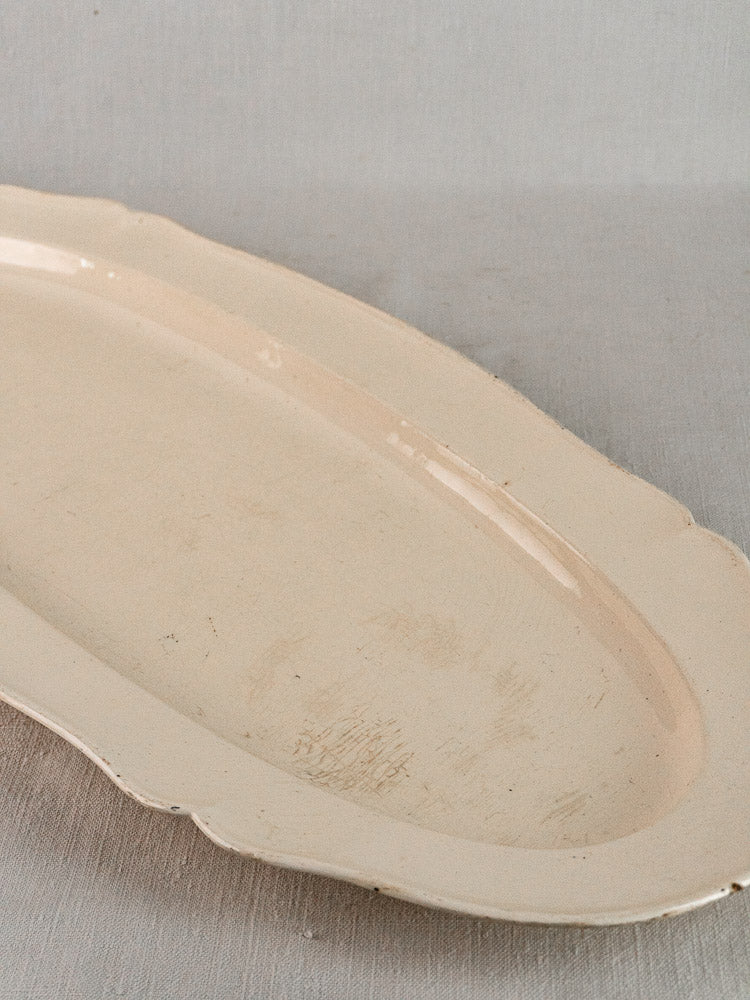 Antique French faience oval meat platter with scalloped edge, early 19th century, on gray surface.