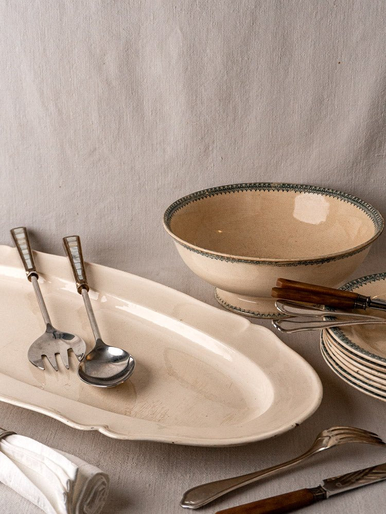 Antique French faience meat platter with vintage ceramic dishes on neutral fabric background.