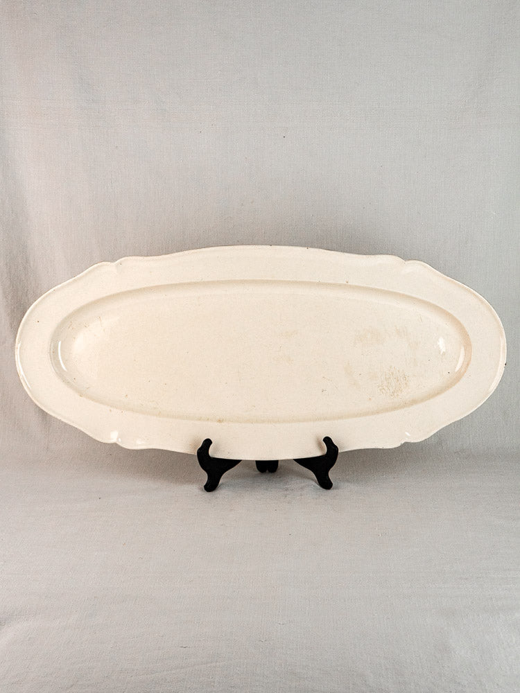 Antique French faience oval meat platter with raised rim on black stand, light background.