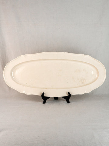 Antique French faience oval meat platter with raised rim on black stand, light background.