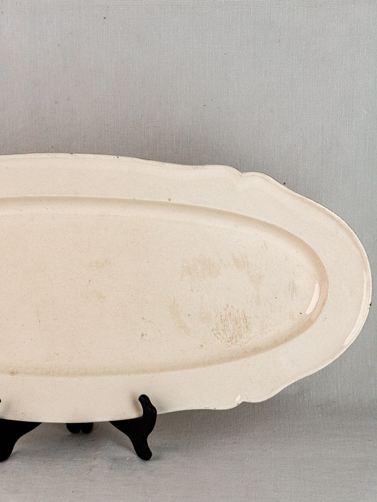 Antique French faience oval ceramic meat platter with raised rim on black stand, light gray background.