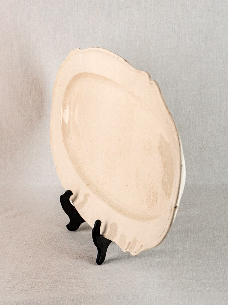 Antique French faience meat platter with scalloped oval shape, upright on a black stand.