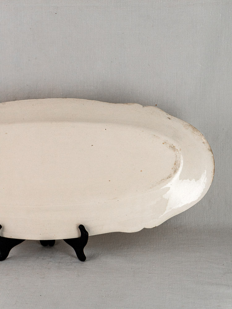 Early 19th-century French faience oval ceramic meat platter with subtle irregular edge on black stand.