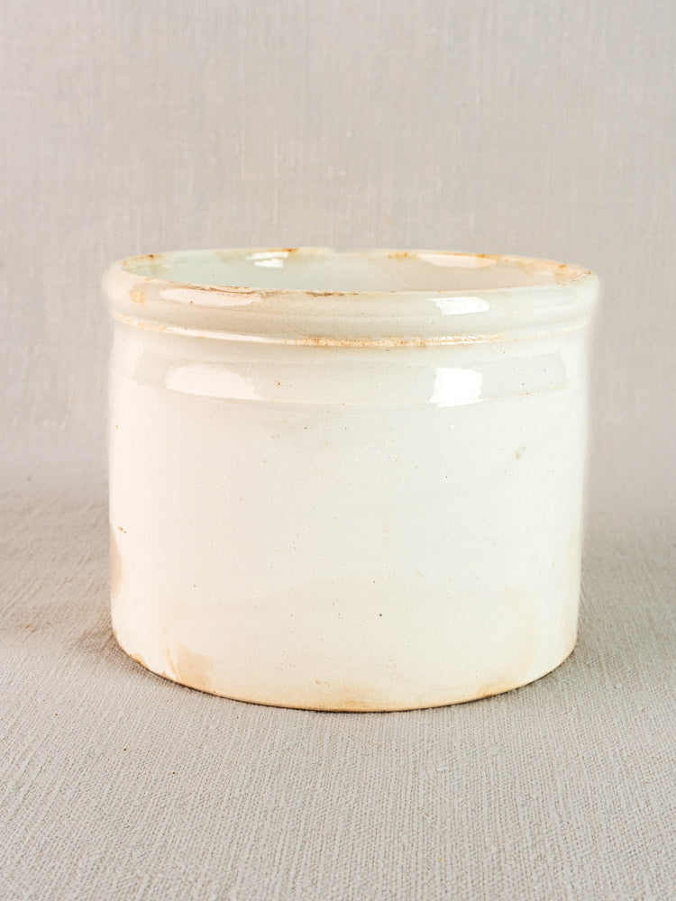 Antique French Fenal Badonviller white ironstone rillettes pot with tan base staining on textured surface.