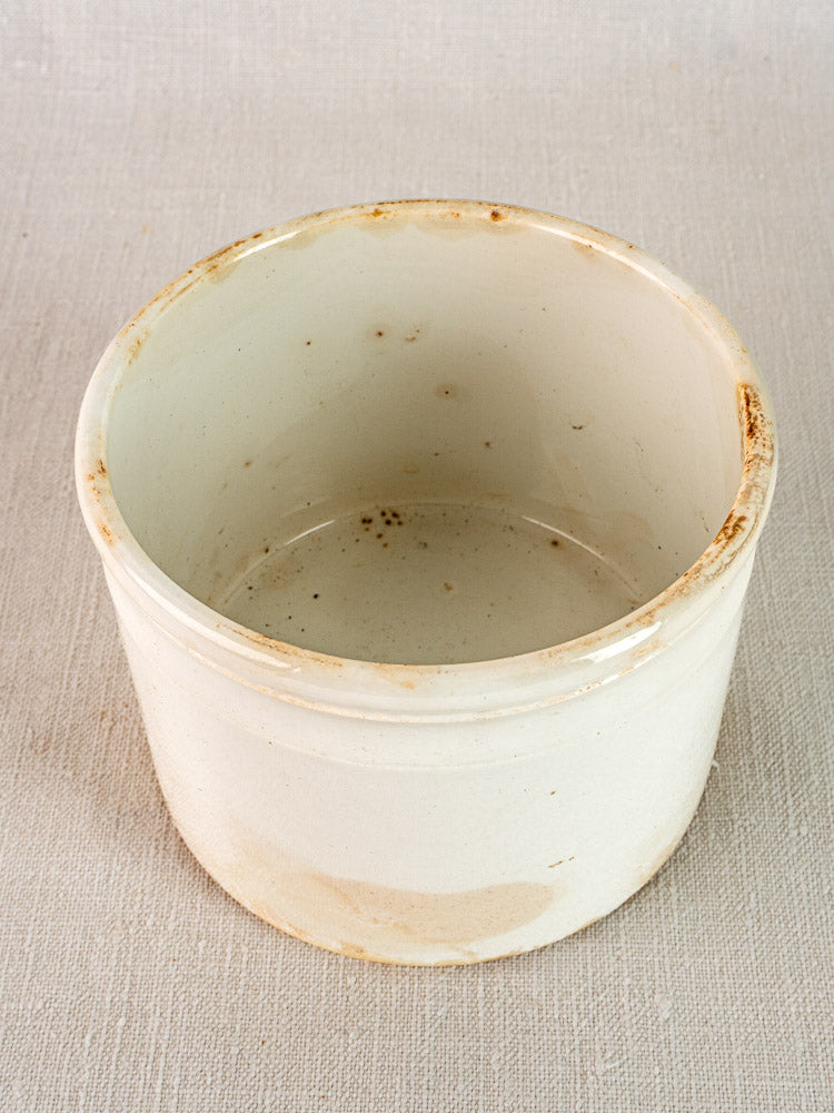 Antique French Fenal Badonviller rillettes pot in white ironstone with visible wear on a light fabric.