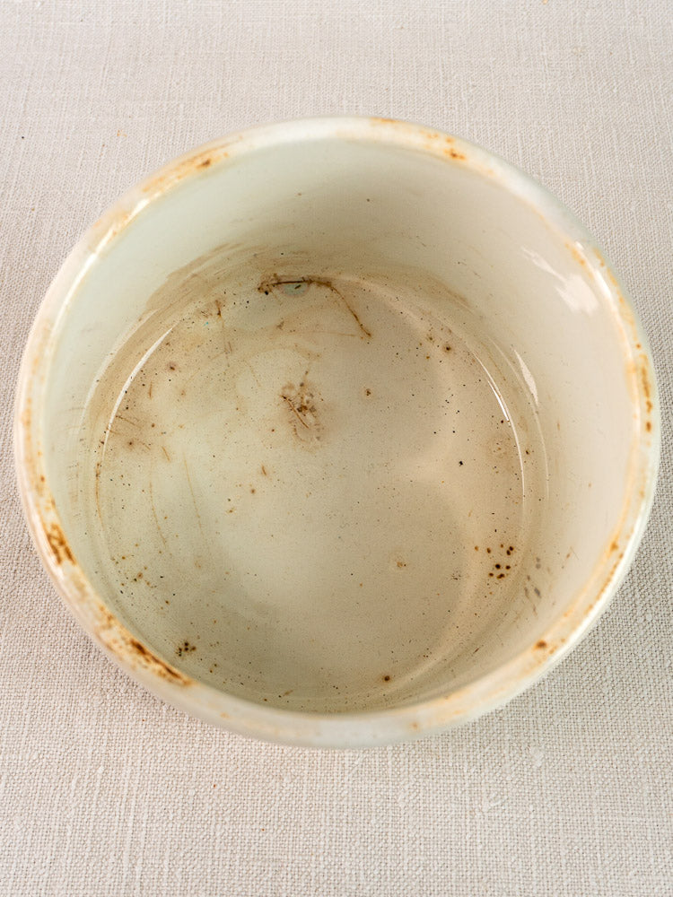 Antique French Fenal Badonviller rillettes pot in white ironstone with brown residue, on off-white surface.